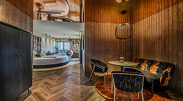 Wohn- und Essbereich der Private Cinema Suite Wohn- und Essbereich der Private Cinema Suite im Hotel Winzer mit gemütlicher Sitzecke, Esstisch und Blick in den Schlafbereich