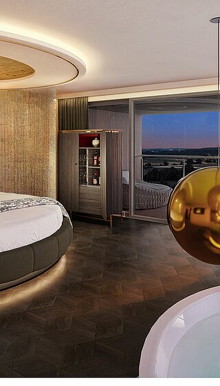 Innenansicht der Hideaway Suite mit Fokus auf das runde Bett mit gemustertem Kopfteil und indirekter Beleuchtung. Im Vordergrund ist der Whirlpool zu sehen, darüber schwebt ein goldener Design-Kamin. Große Fensterfronten bieten einen weiten Blick in die Landschaft.