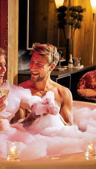 A couple in the hot tub with champagne in the cosy suite at the Hotel Winzer
