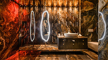 Badezimmer der Wolke 7 Luxuriöses Badezimmer der Wolke 7 im Hotel Winzer mit Naturstein, elegantem Waschtisch, beleuchteten Spiegeln und stimmungsvoller Beleuchtung