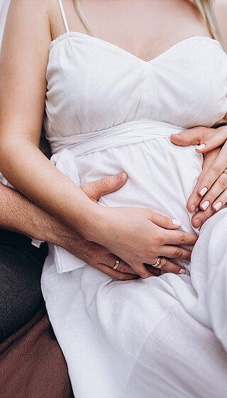 Schwangere Frau und ihr Mann die ihren Bauch umarmen