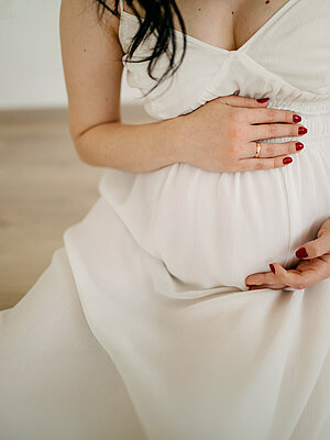 Schwangere Frau in weißem Kleid die ihren Bauch umarmt