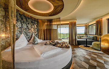 Sleeping area in the Hideaway Suite at Hotel Winzer with a round double bed, cosy living area, balcony and freestanding fireplace