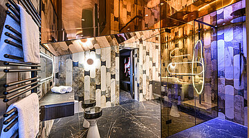 Badezimmer mit Glasdusche Luxuriöses Badezimmer im Hotel Winzer mit großflächiger Glasdusche, Natursteinoptik, beleuchteten Spiegeln und modernem Waschtisch