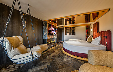 Sleeping area in the Secret Love Suite at Hotel Winzer with a round double bed, hanging chair and contemporary fireplace