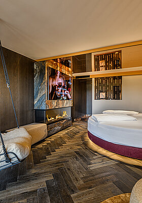 Sleeping Area with Fireplace Sleeping area in the Secret Love Suite at Hotel Winzer with a round double bed, hanging chair and contemporary fireplace