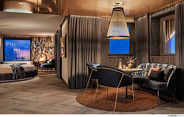 Luxuriöse Private Cinema Suite mit rundem Bett, elegantem Essbereich und kupferfarben glänzender Decke.