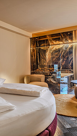 Schlafbereich der Juniorsuite Kuscheltraum Deluxe Schlafbereich der Juniorsuite Kuscheltraum Deluxe im Hotel Winzer mit rundem Doppelbett, Kamin, Wohnbereich und Balkon