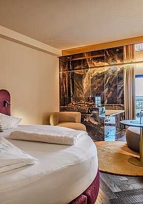 Schlafbereich der Juniorsuite Kuscheltraum Deluxe im Hotel Winzer mit rundem Doppelbett, Kamin, Wohnbereich und Balkon